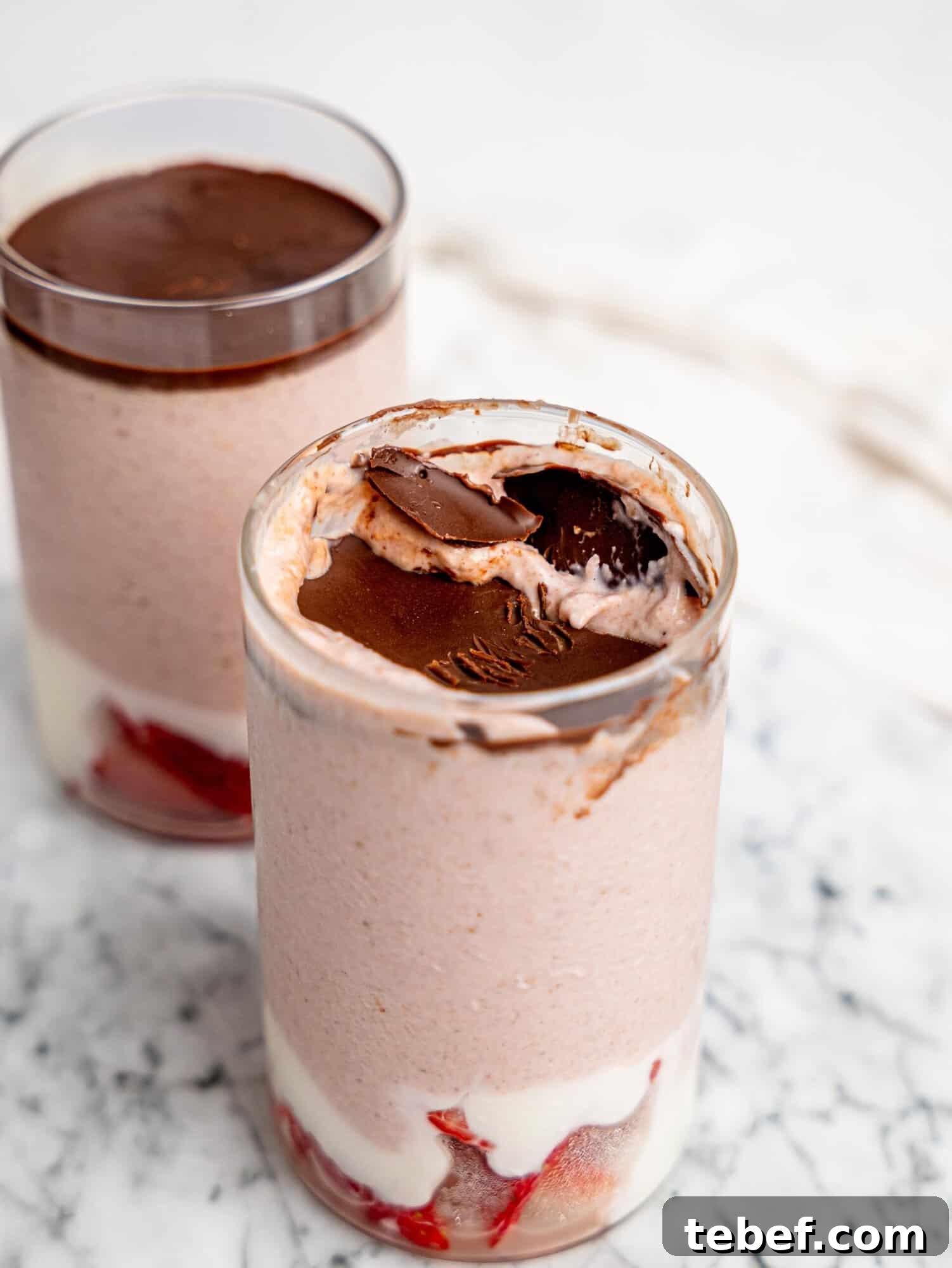 Close-up of strawberry blended overnight oats topped with a set chocolate layer that has been cracked, revealing the creamy oat mixture underneath.