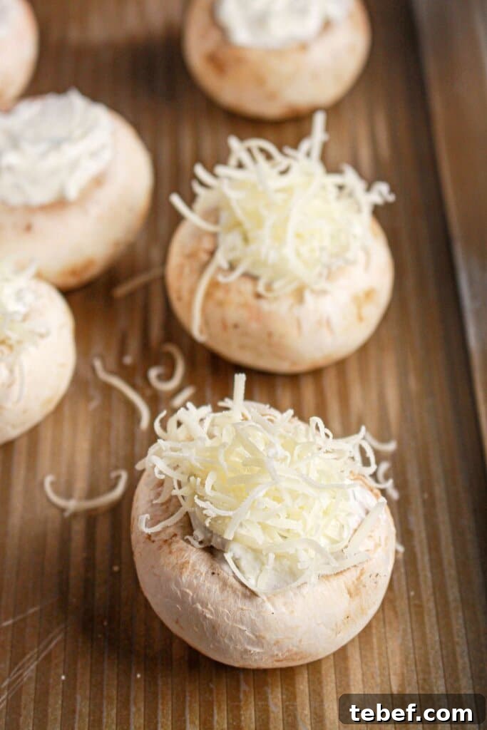 Cream Cheese Stuffed Mushrooms Recipe with Garlic and Herbs 8 Parmesan cheese being sprinkled on top of caps on a baking dish.