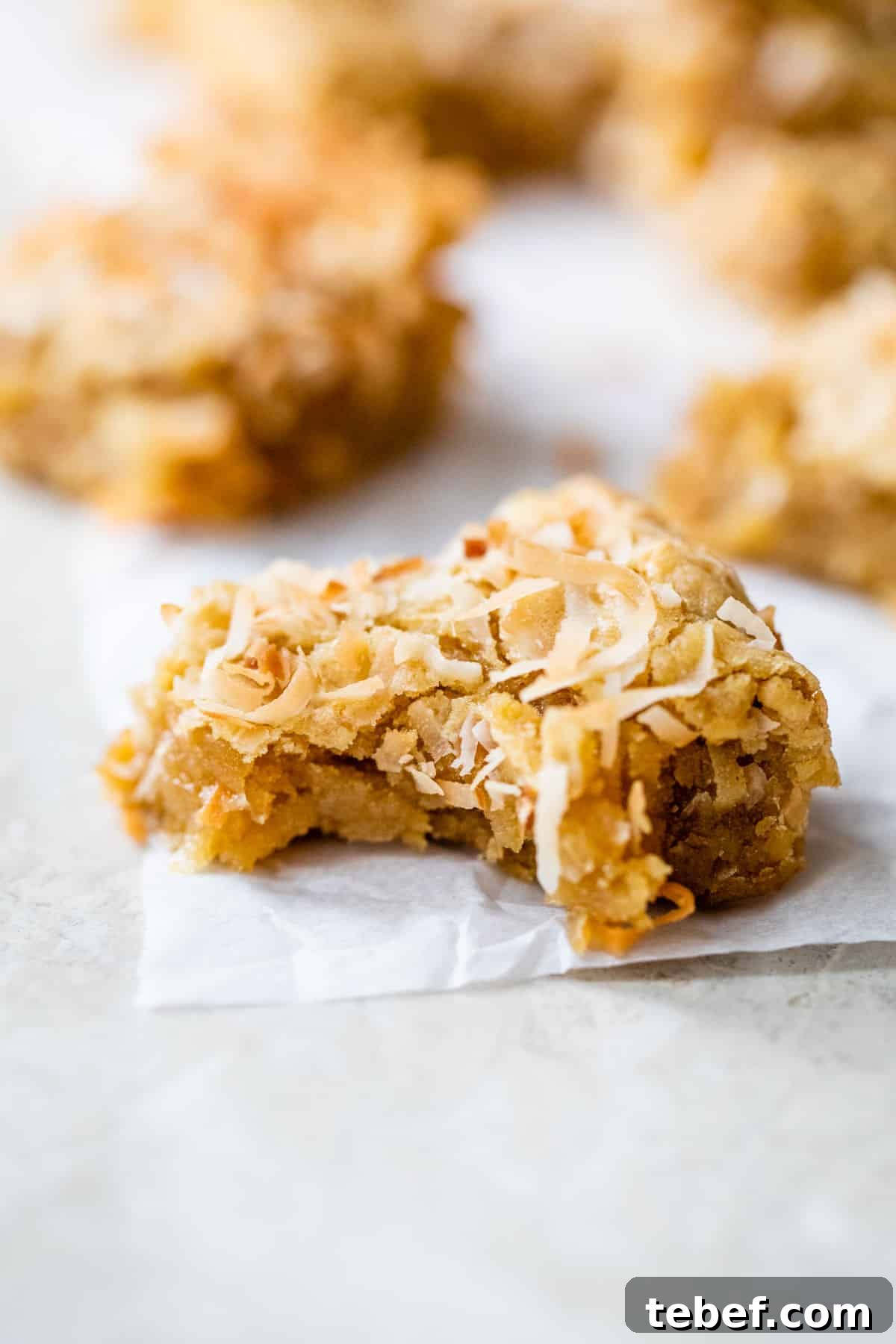 Buttery Coconut Bars Recipe with Crisp Shortbread Crust 6 bar topped with coconut with a bite taken out of it