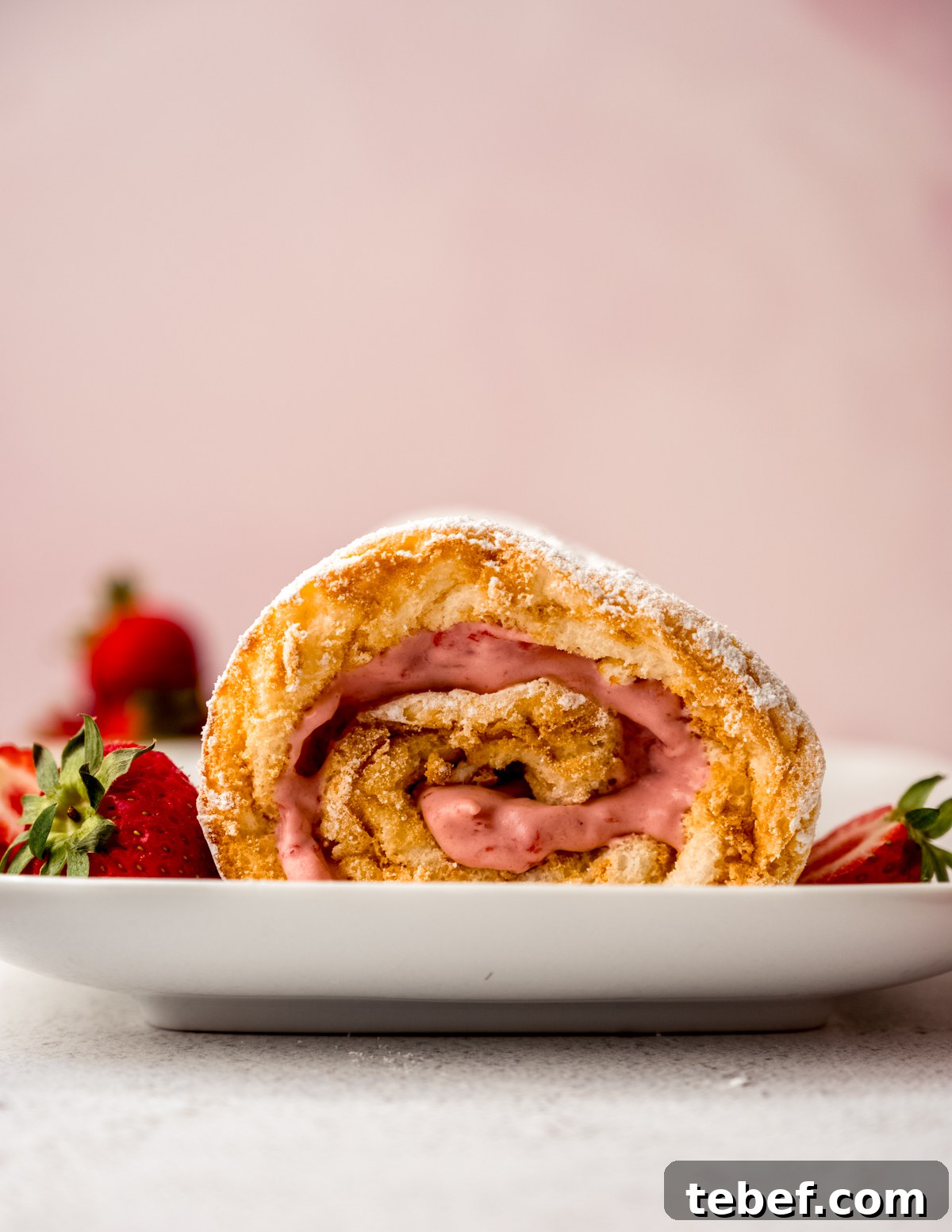 Decadent Strawberry Swiss Roll Recipe with Cream Filling 2 A strawberry Swiss roll cake on a plate with strawberries around it.