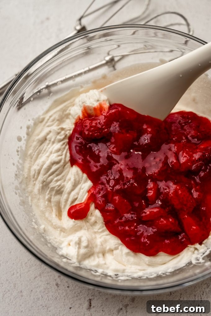 Decadent Strawberry Swiss Roll Recipe with Cream Filling 16 A bowl of whipped cream with strawberry puree and a spatula in it.