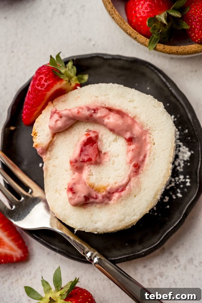 Decadent Strawberry Swiss Roll Recipe with Cream Filling 3 A slice of strawberry Swiss roll cake on a plate with a fork.