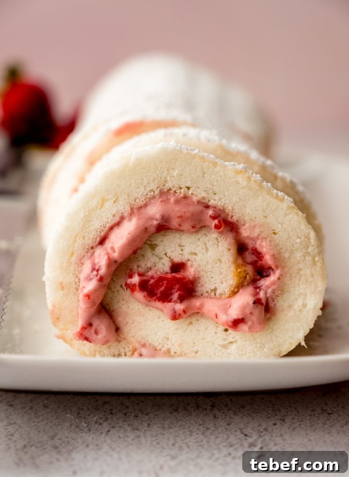 Decadent Strawberry Swiss Roll Recipe with Cream Filling 19 A strawberry Swiss roll cake on a plate with strawberries around it.