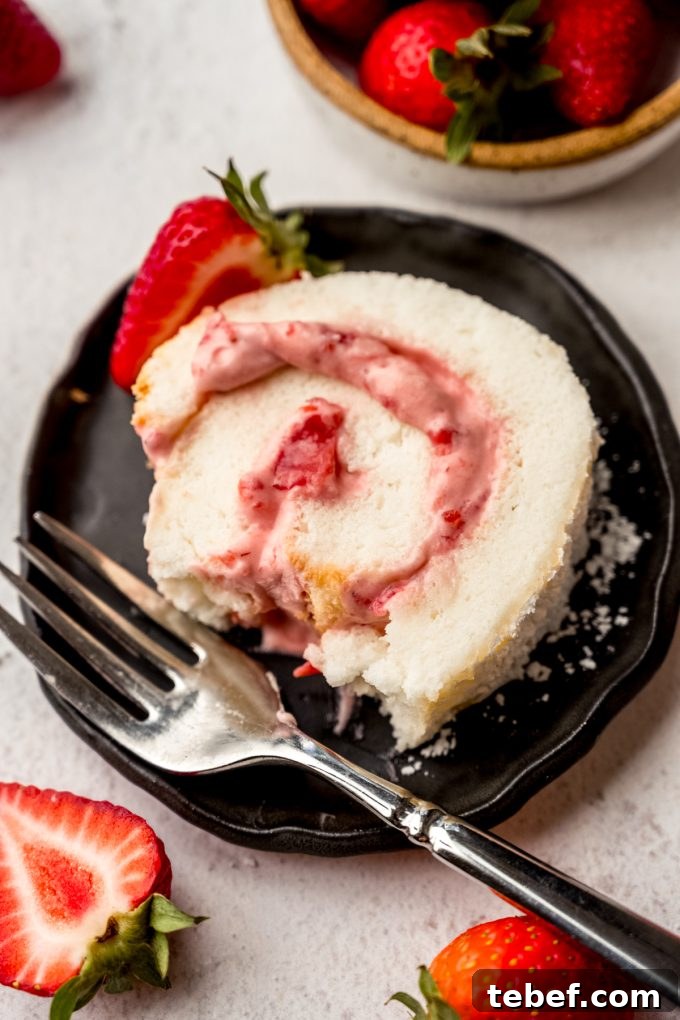 Decadent Strawberry Swiss Roll Recipe with Cream Filling 21 A slice of strawberry Swiss roll cake on a plate with a bite taken out of it.