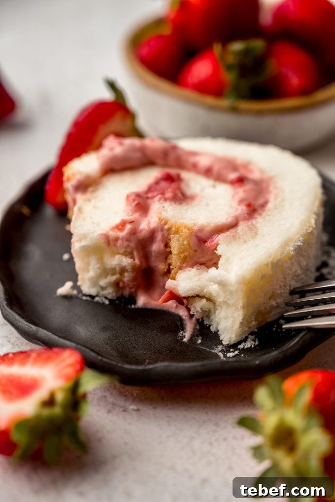 Decadent Strawberry Swiss Roll Recipe with Cream Filling 4 A slice of strawberry Swiss roll cake on a plate with a bite taken out of it.