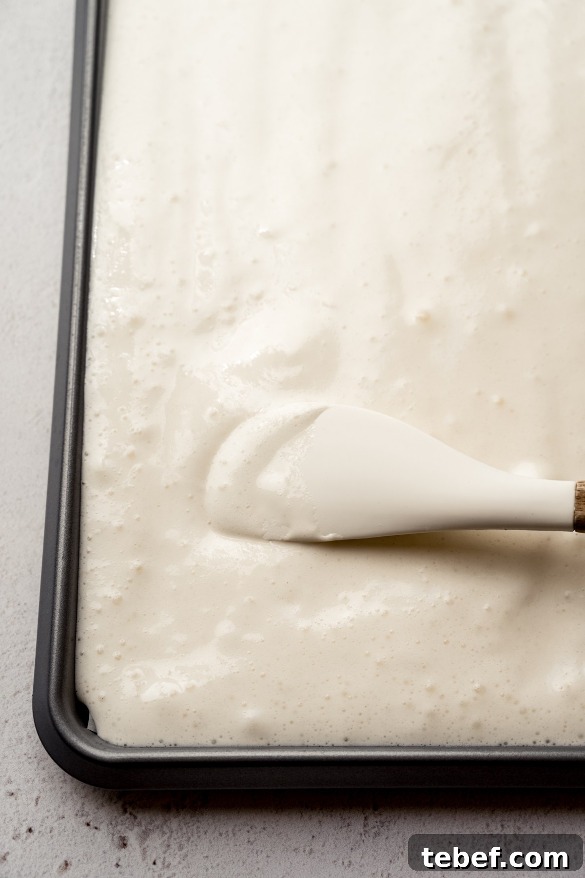 Decadent Strawberry Swiss Roll Recipe with Cream Filling 9 Someone is using a spatula to spread cake batter into a jelly roll pan.