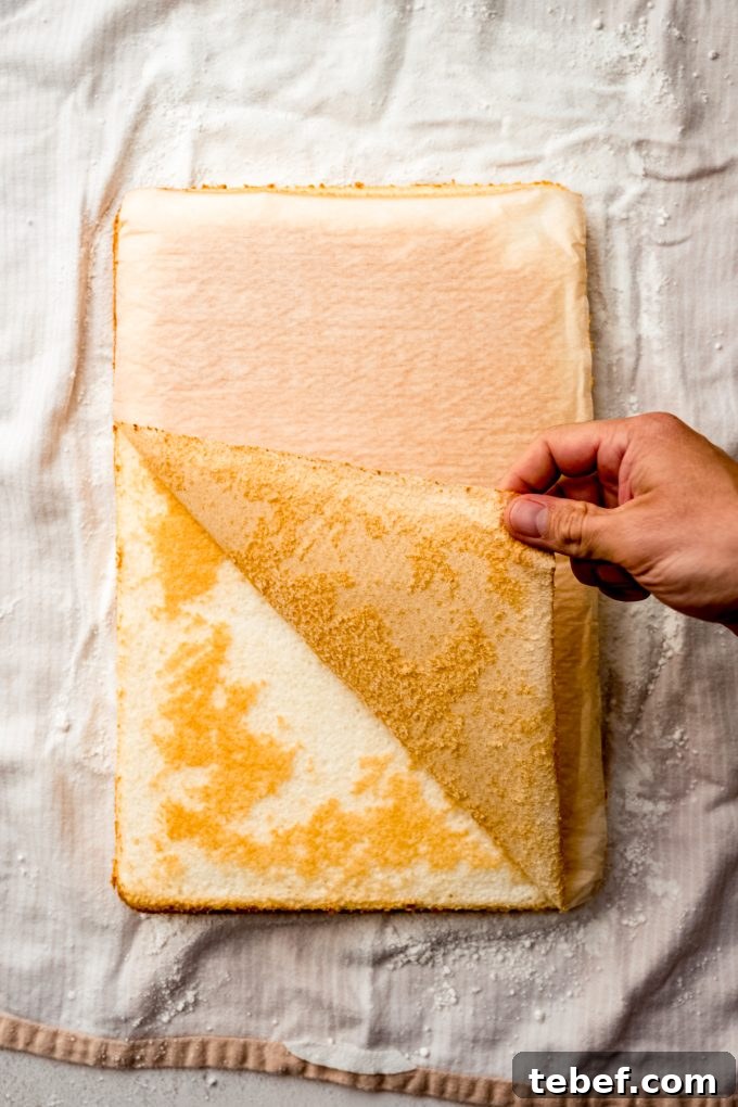 Decadent Strawberry Swiss Roll Recipe with Cream Filling 10 Someone is pulling the parchment off of a layer of cake to make a Swiss cake roll.