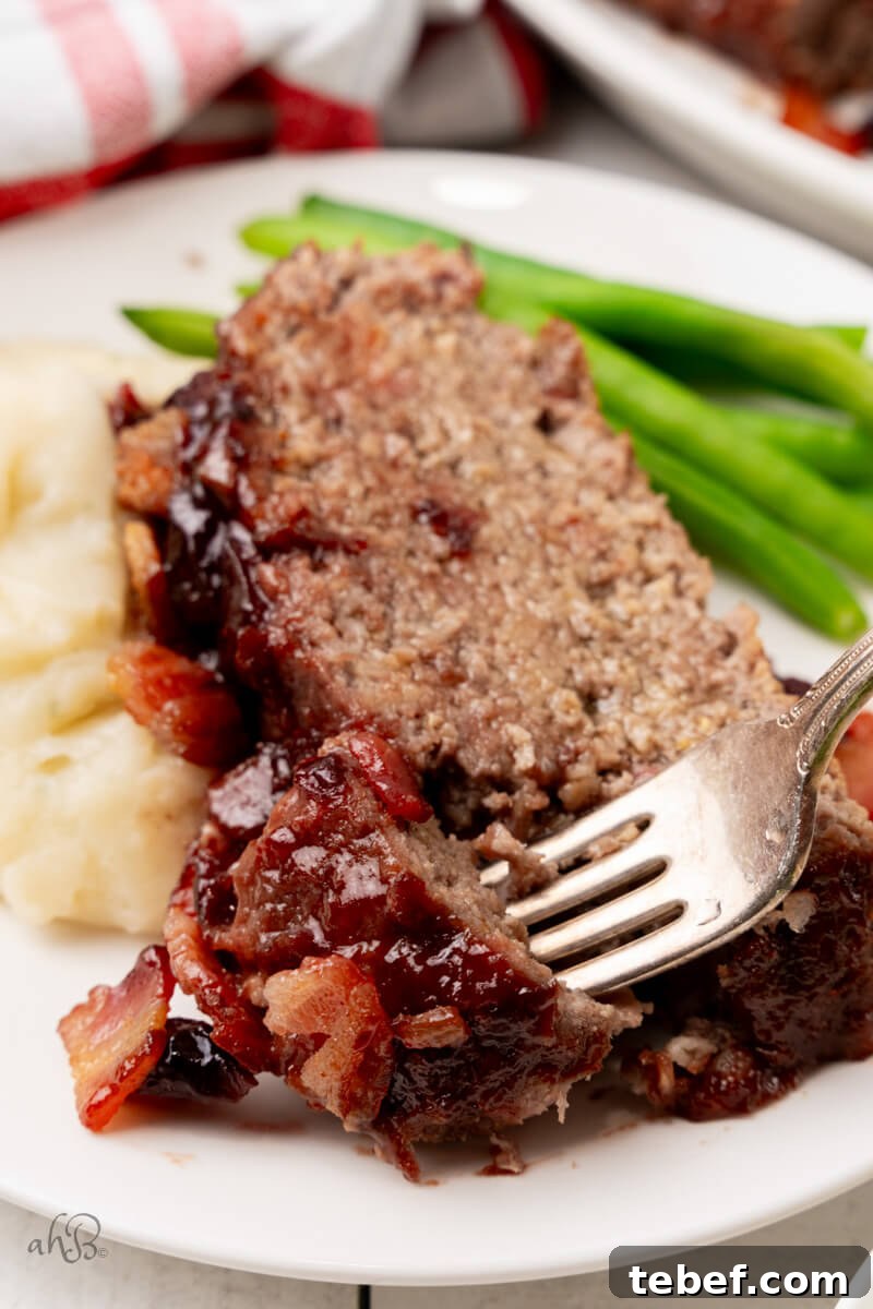 Bacon Bourbon Meatloaf-30 A slice of bourbon bacon meatloaf served with mashed potatoes and green beans is stabbed with a fork.
