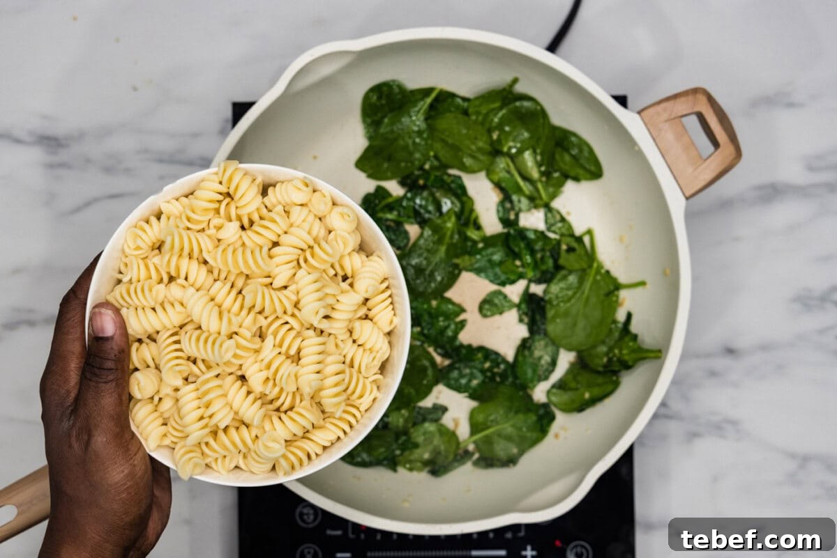 Creamy Basil Pesto Pasta with Parmesan and Pine Nuts 6 adding pasta to spinach in a skillet