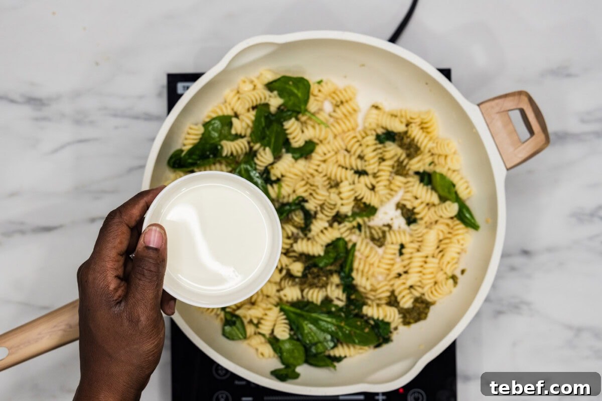 Creamy Basil Pesto Pasta with Parmesan and Pine Nuts 7 adding heavy cream to skillet with spinach and pasta