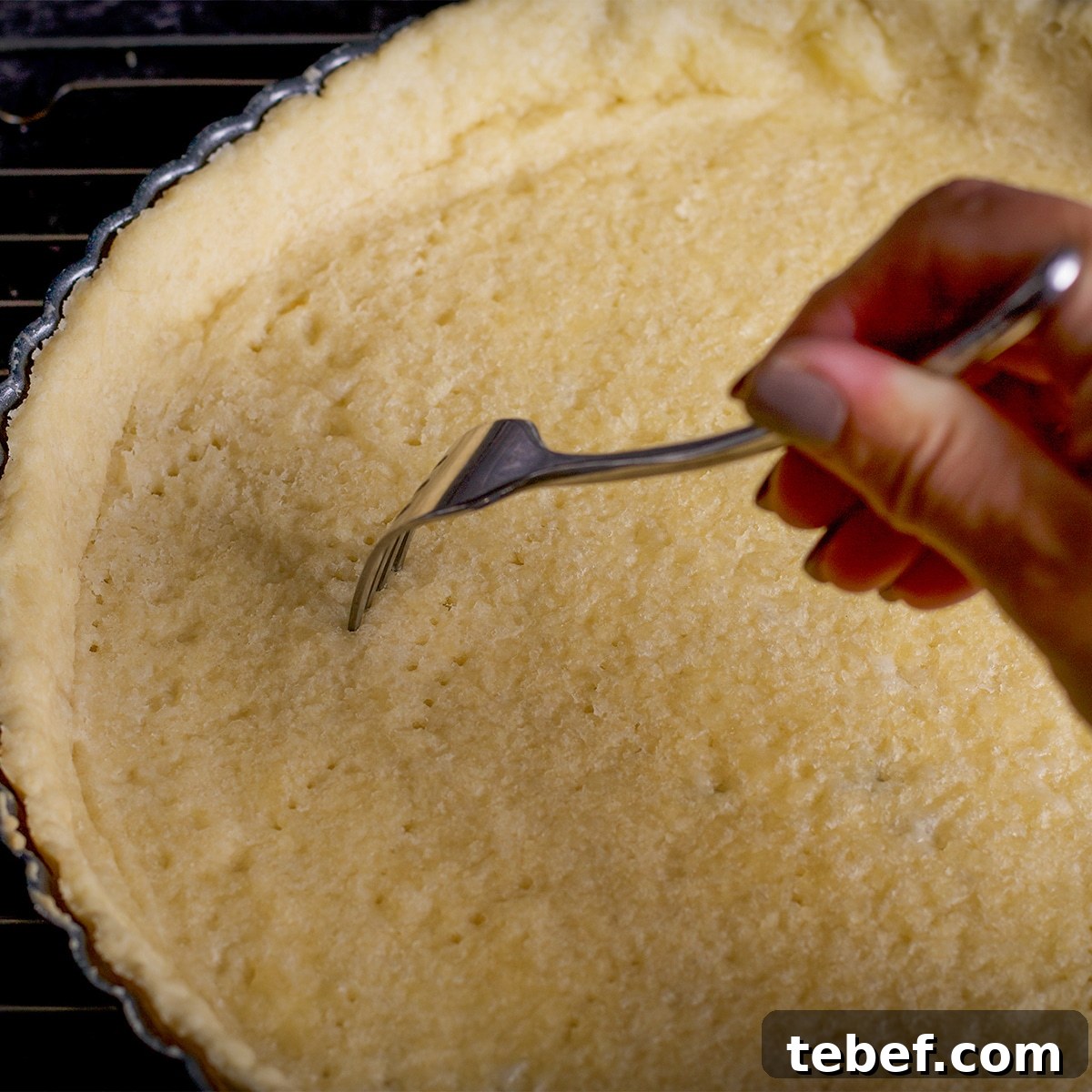 Someone using a fork to poke holes in tart crust dough.