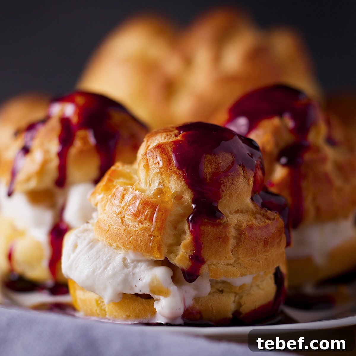 A tray of ice cream filled profiteroles that have been drizzled with red wine dessert sauce.