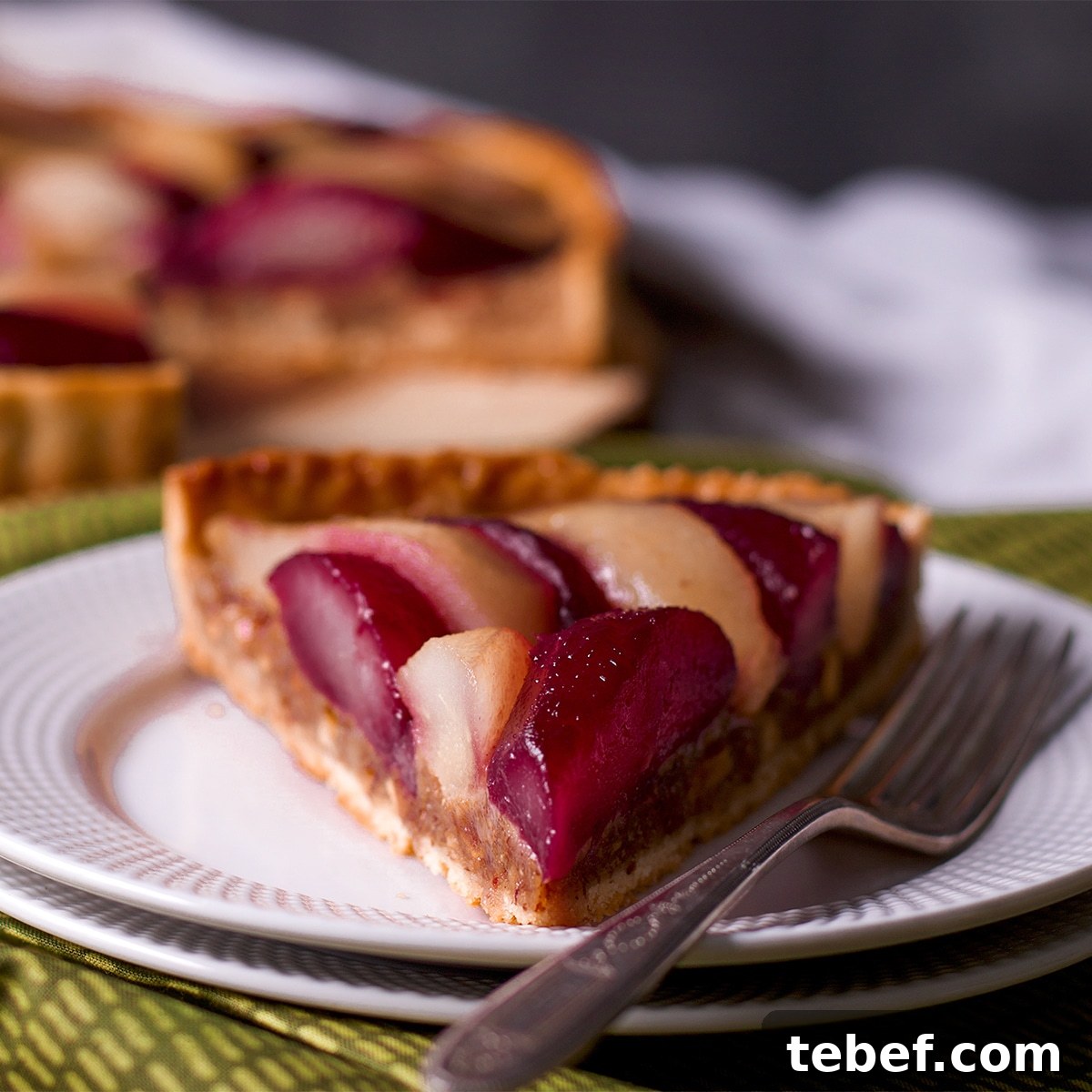A slice of poached pear and frangipane tart on a white plate with a fork.