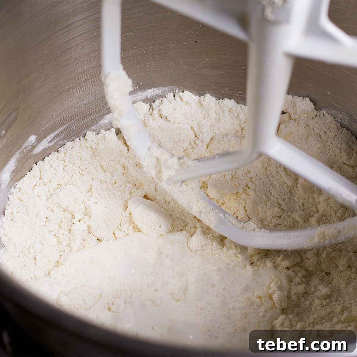 Adding cream to the flour and butter mixture as it mixes together in the bowl of a stand mixer.
