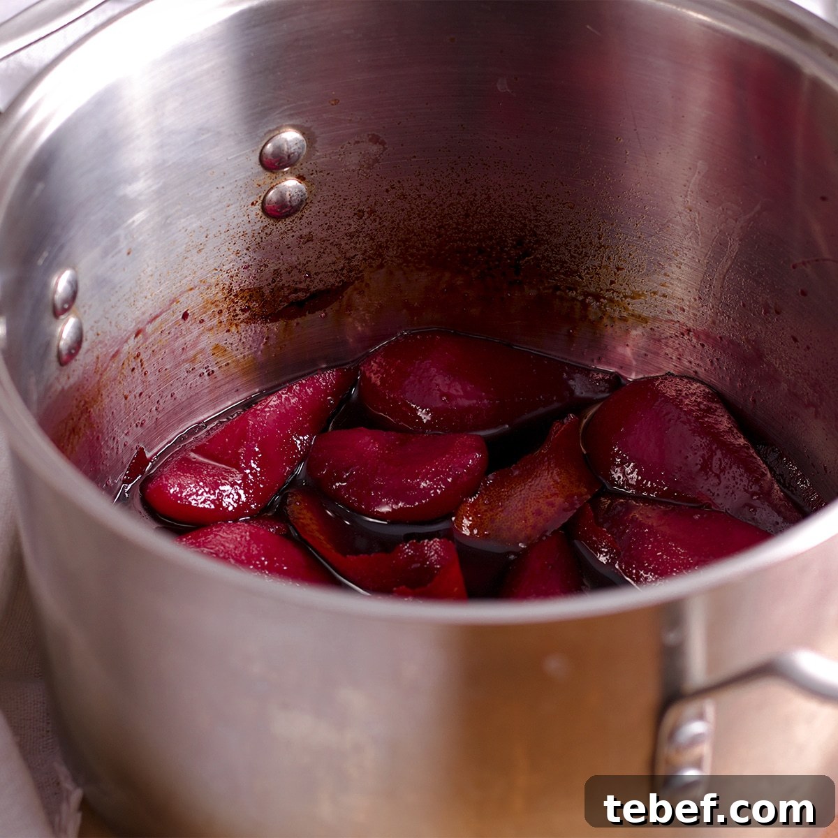 A saucepan containing pears poaching in red wine.
