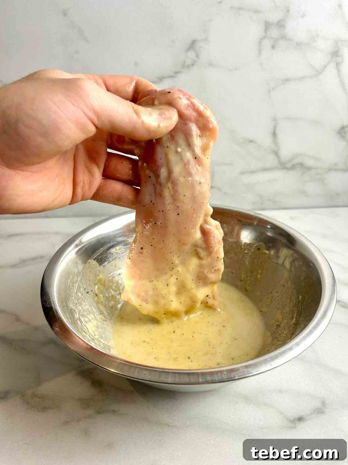Chicken Katsu Musubi Recipe: How to Make Japanese Fried Chicken Rice Balls 8 hand lifting chicken thigh from bowl of dredge