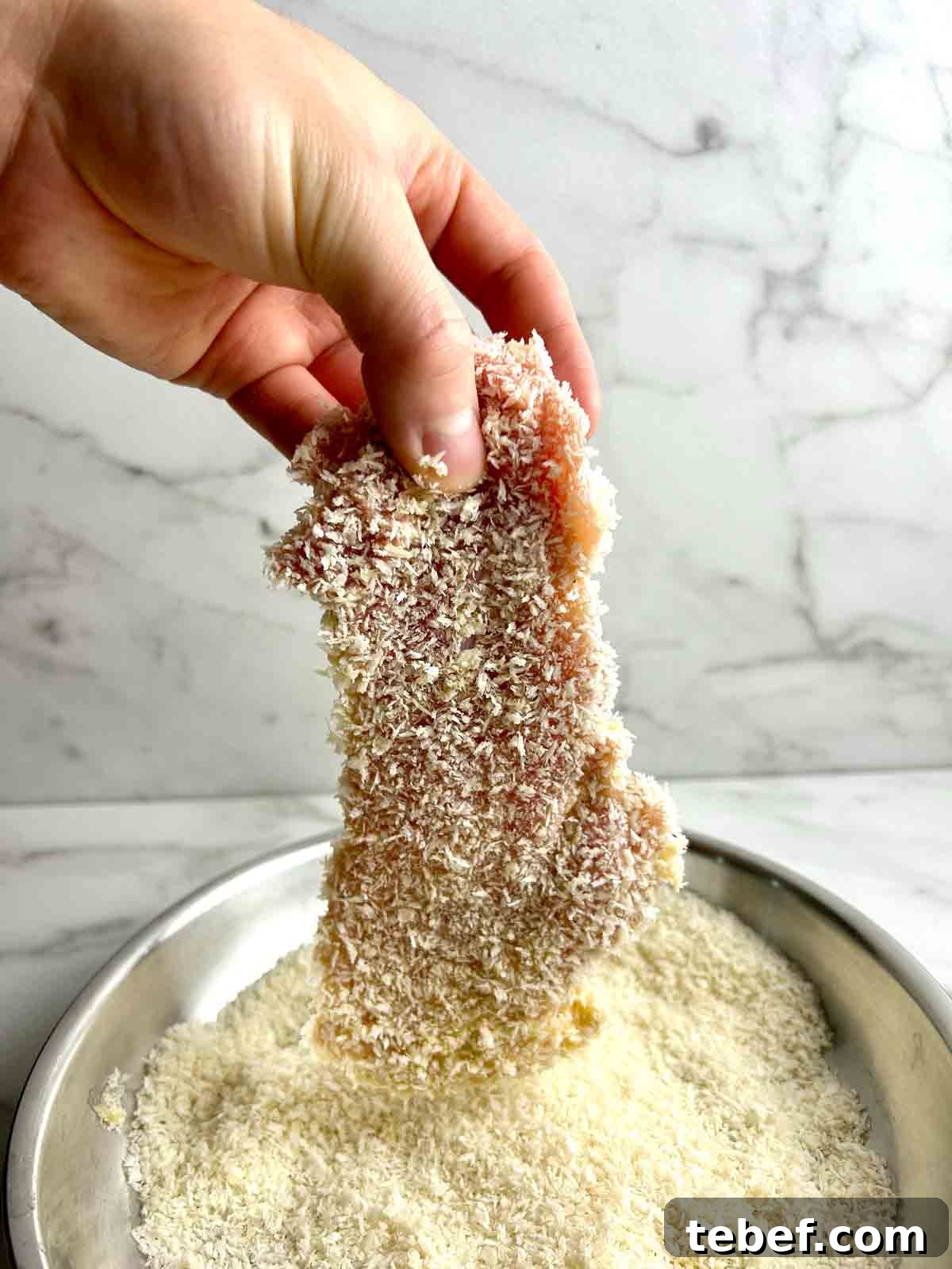 Chicken Katsu Musubi Recipe: How to Make Japanese Fried Chicken Rice Balls 9 hand lifting breaded chicken thigh from bowl of breadcrumbs