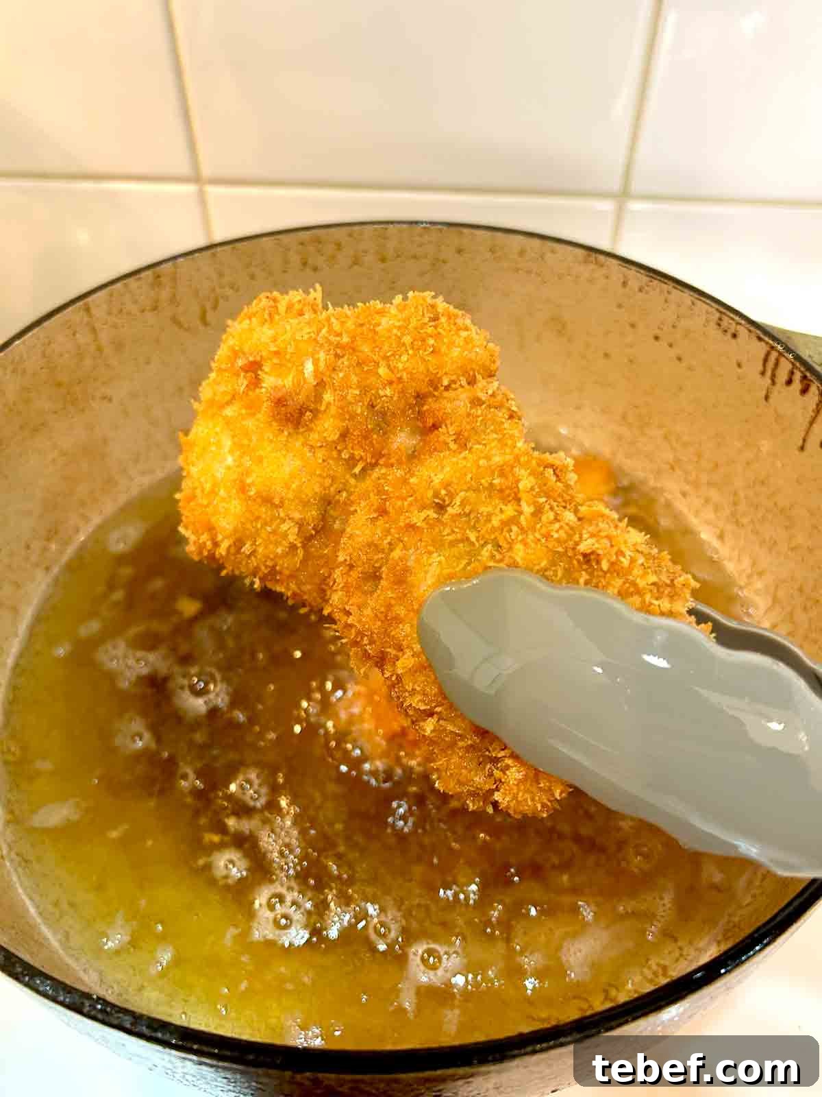 Chicken Katsu Musubi Recipe: How to Make Japanese Fried Chicken Rice Balls 10 chicken katsu being lifted out of fryer with tongs