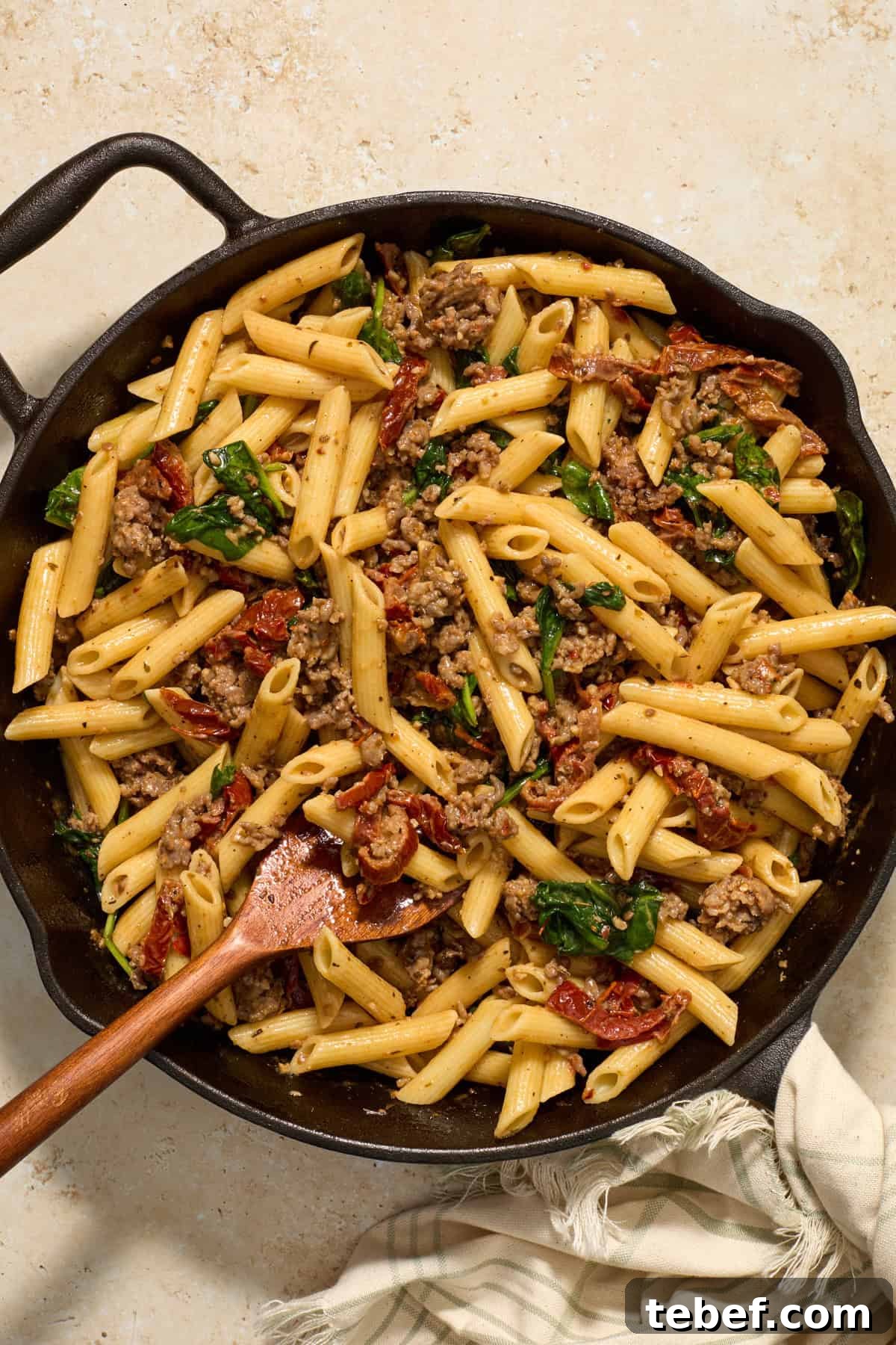 Sun-Dried Tomato Pasta with Savory Italian Sausage 10 Sun-dried tomato and Italian sausage pasta tossed together with wood spoon in cast iron skillet.