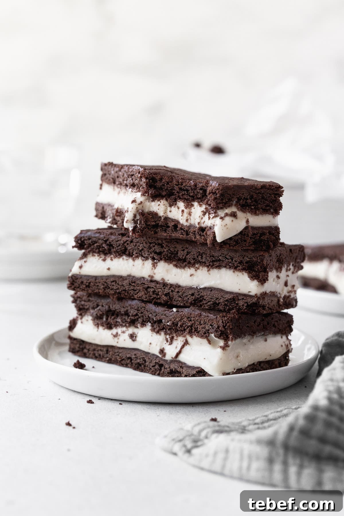 A stack of ice cream sandwich cookies on a small white dish with a large bite taken out of one of the cookies.