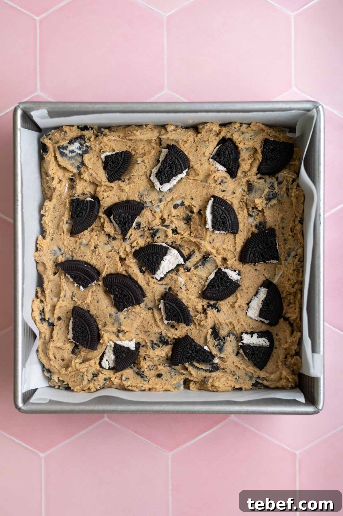 oreo cookies broken and pressed into the top of the bar cookie dough in a baking pan