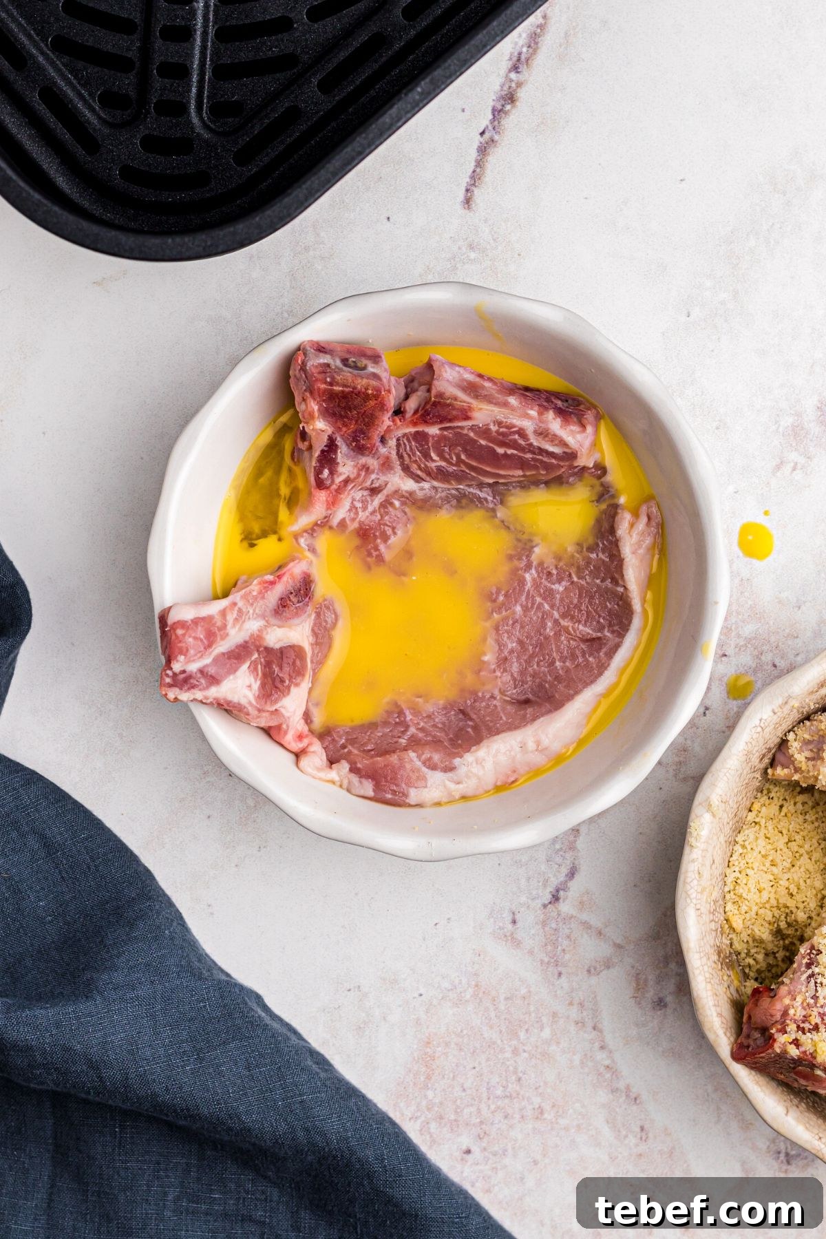 Crispy Gluten-Free Pork Chops in the Air Fryer 5 White shallow dish with pork chop being soaked in whisked egg
