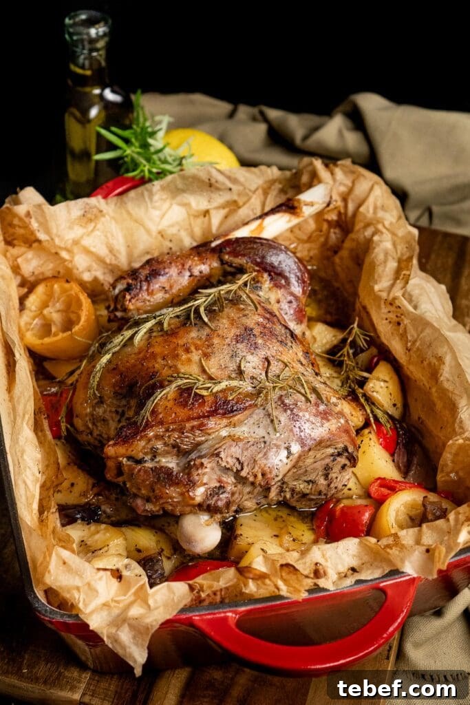 A roasted whole leg of lamb kleftiko sat on top of potatoes, peppers and onions. In a parchment lined a roasting tray.