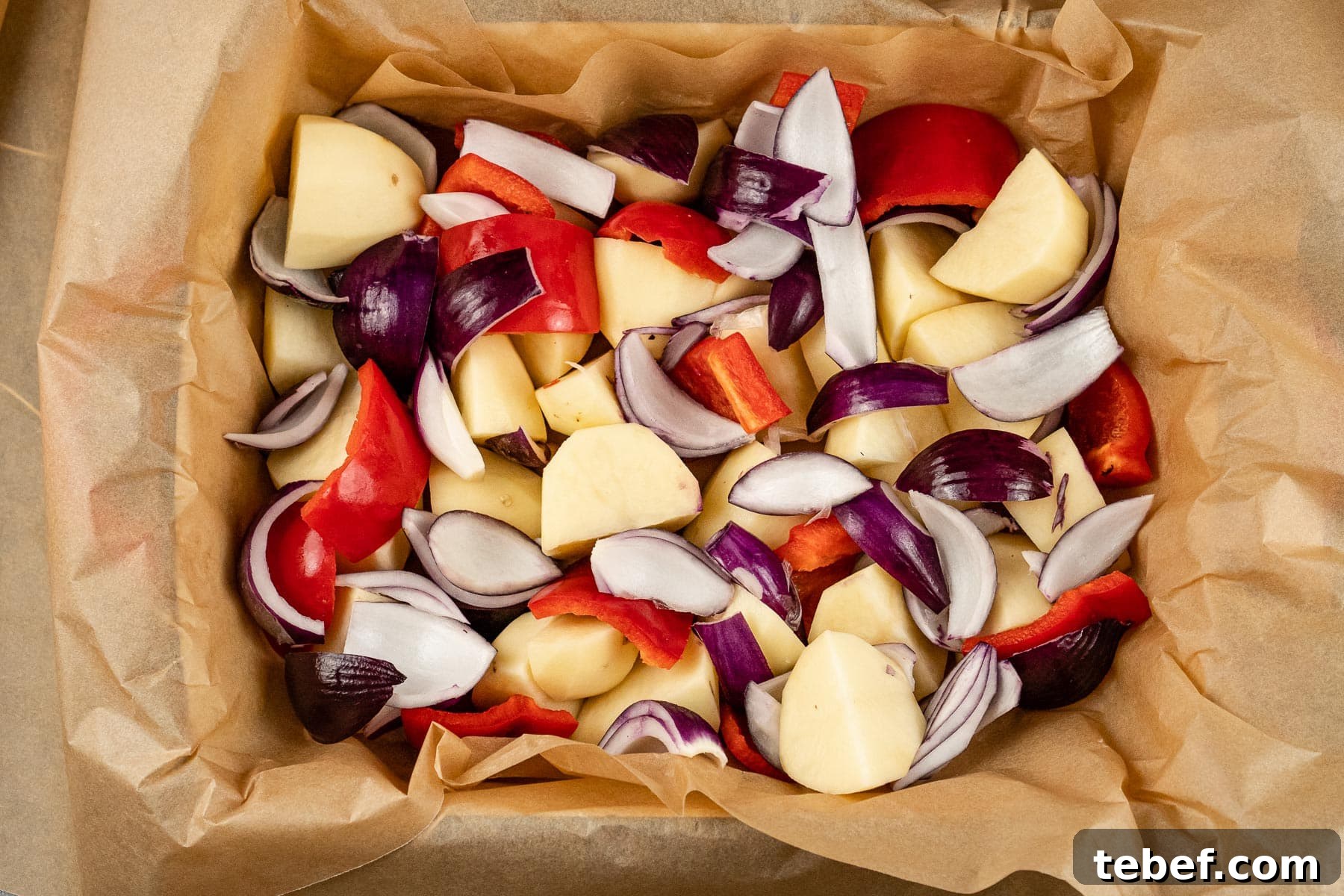 Potatoes, red onions and red peppers chopped and placed in a roasting dish lined with parchment paper