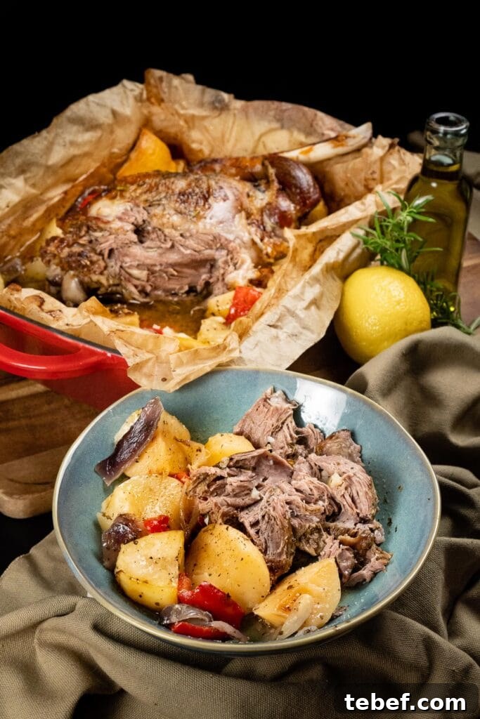 Lamb kleftiko served in a blue bowl with lemon potatoes and vegetables. Leg of lamb can be seen in the background where the meat falls of the bone.
