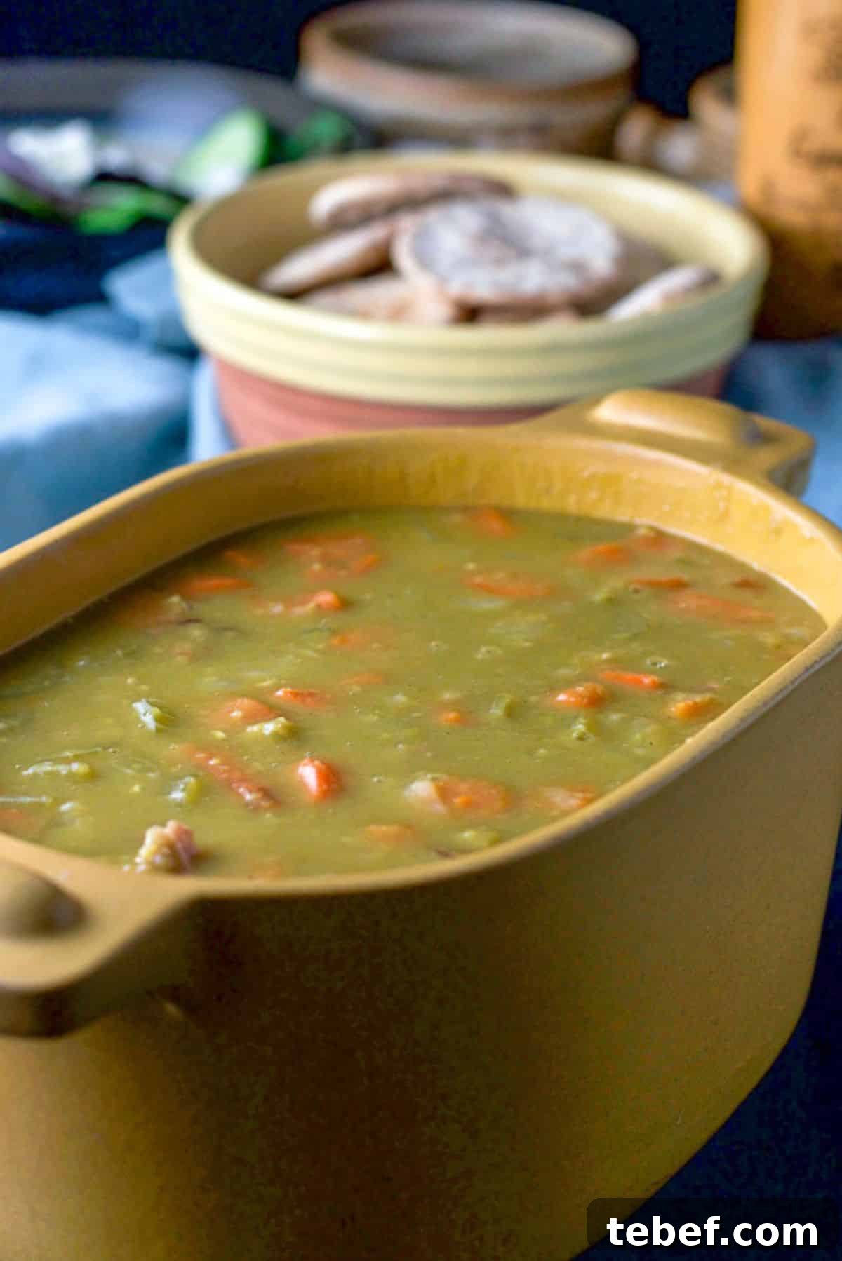 Instant Pot Split Pea Soup Recipe – Creamy, Hearty & Ready Fast 6 A mustard colored casserole dish filled with pea soup. There are some pita bread in a bowl, a salad and a pepper mill in the background