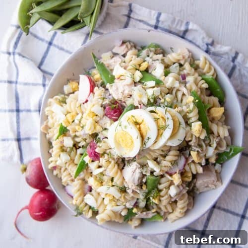 white bowl filled with tuna pasta salad sitting on a white and blue tea towel.