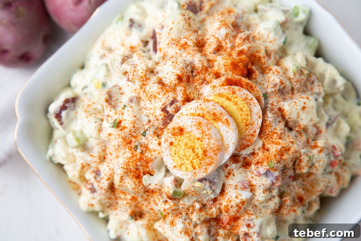 Creamy Red Potato Salad with Tangy Dill Dressing 4 red potato salad in a white dish, topped with a hard boiled egg and paprika.