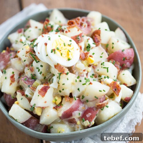 German potato salad with hard boiled eggs and chives in a green bowl on a wooden table