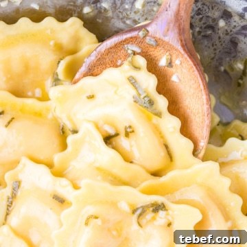 Lobster Ravioli coated in a garlic, butter, sage, and white wine sauce in a pan with a wooden spoon.