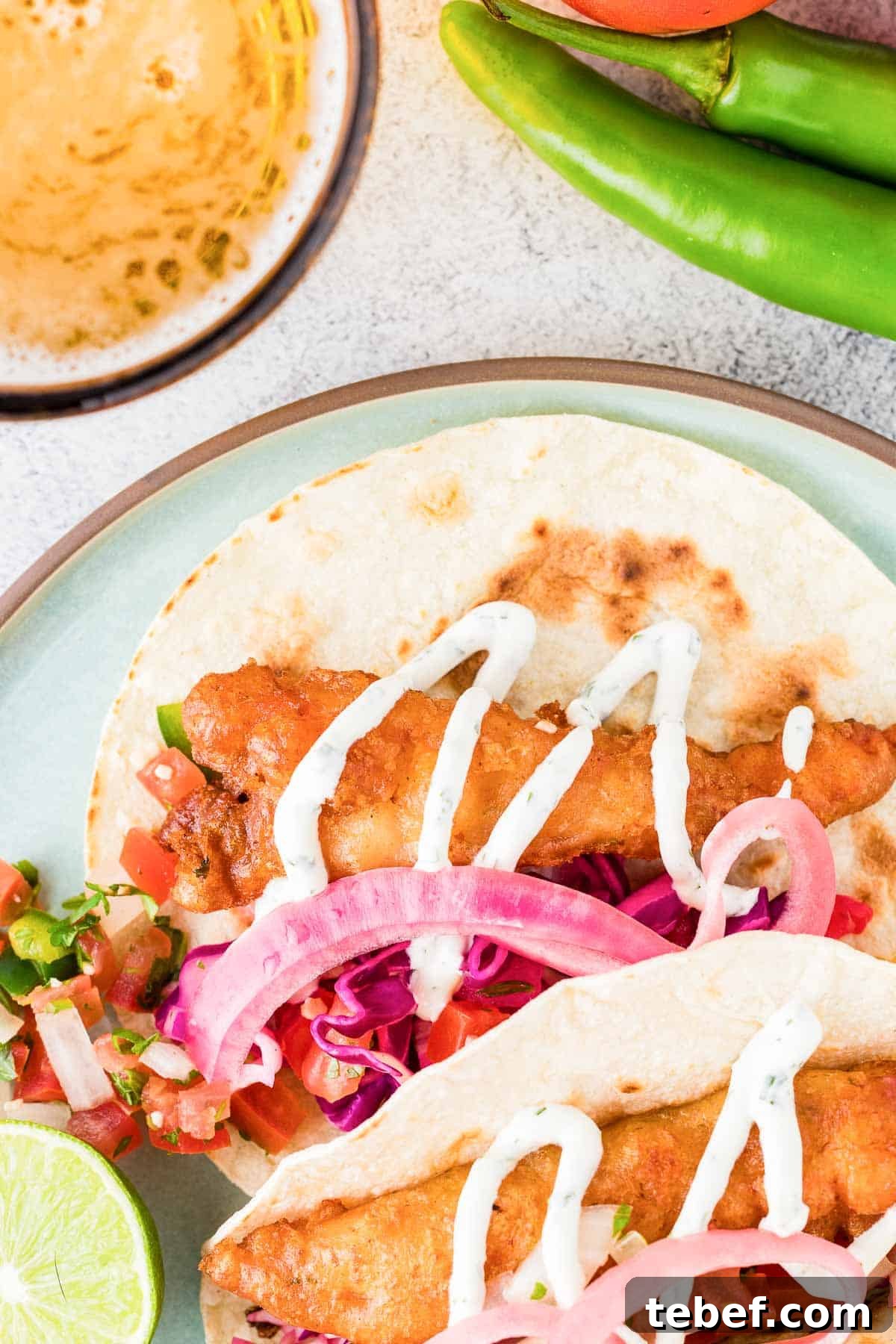 Crispy Beer-Battered Shrimp Recipe — Crunchy Fried Shrimp Guide 8 Beer-battered shrimp tacos garnished with sliced red onions and a drizzle of sauce, accompanied by a slice of lime and fresh jalapeños on the side.