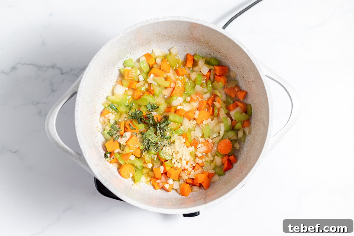 Hearty Chicken and Potato Soup Recipe for Cozy Weeknights 6 Vegetables and herbs are sauteed in a large pot.