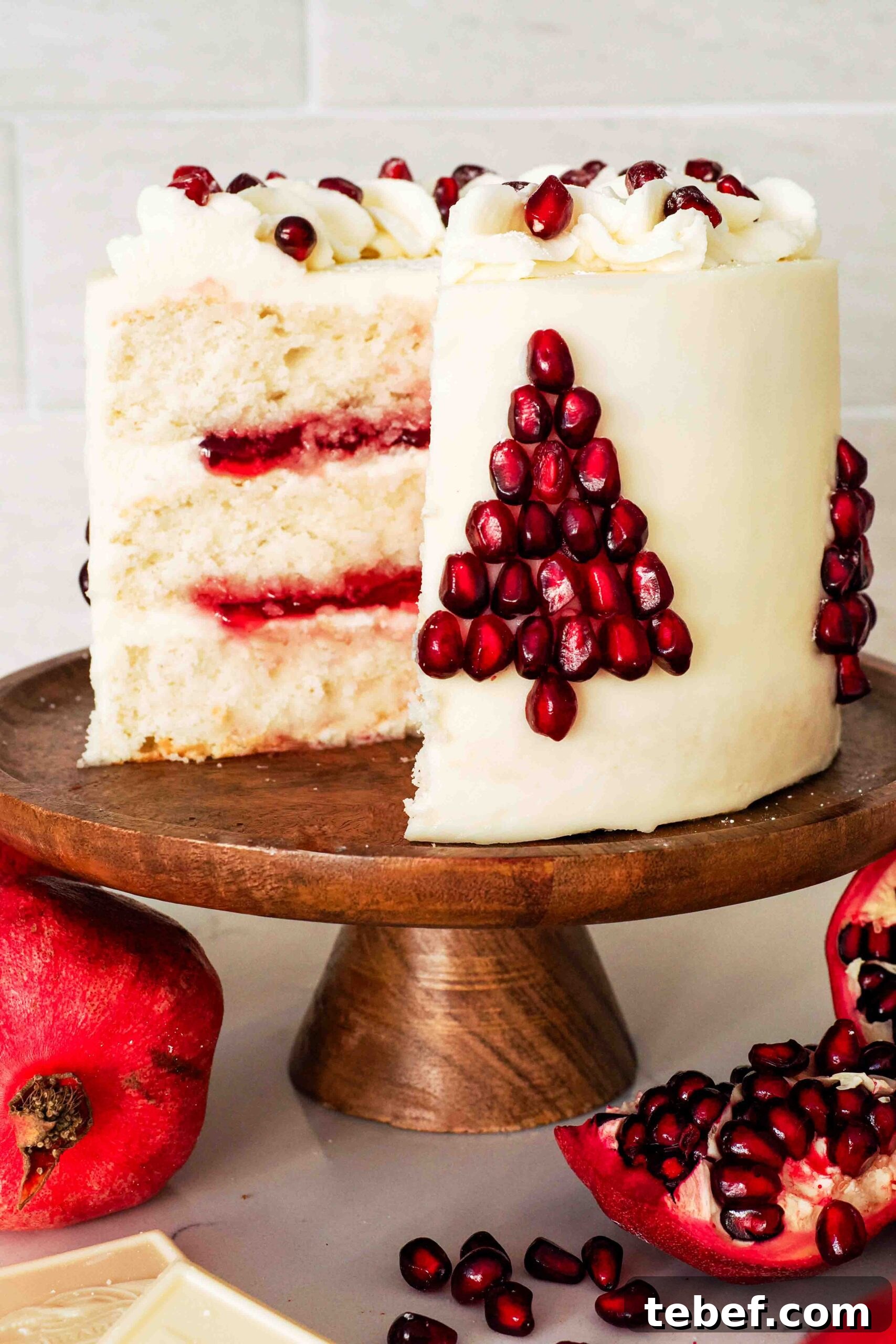 White Chocolate and Pomegranate Layer Cake Recipe 2 A white layer cake filled with pomegranate jelly, frosted with white chocolate buttercream, and decorated with pomegranate seeds in the shape of a Christmas tree.