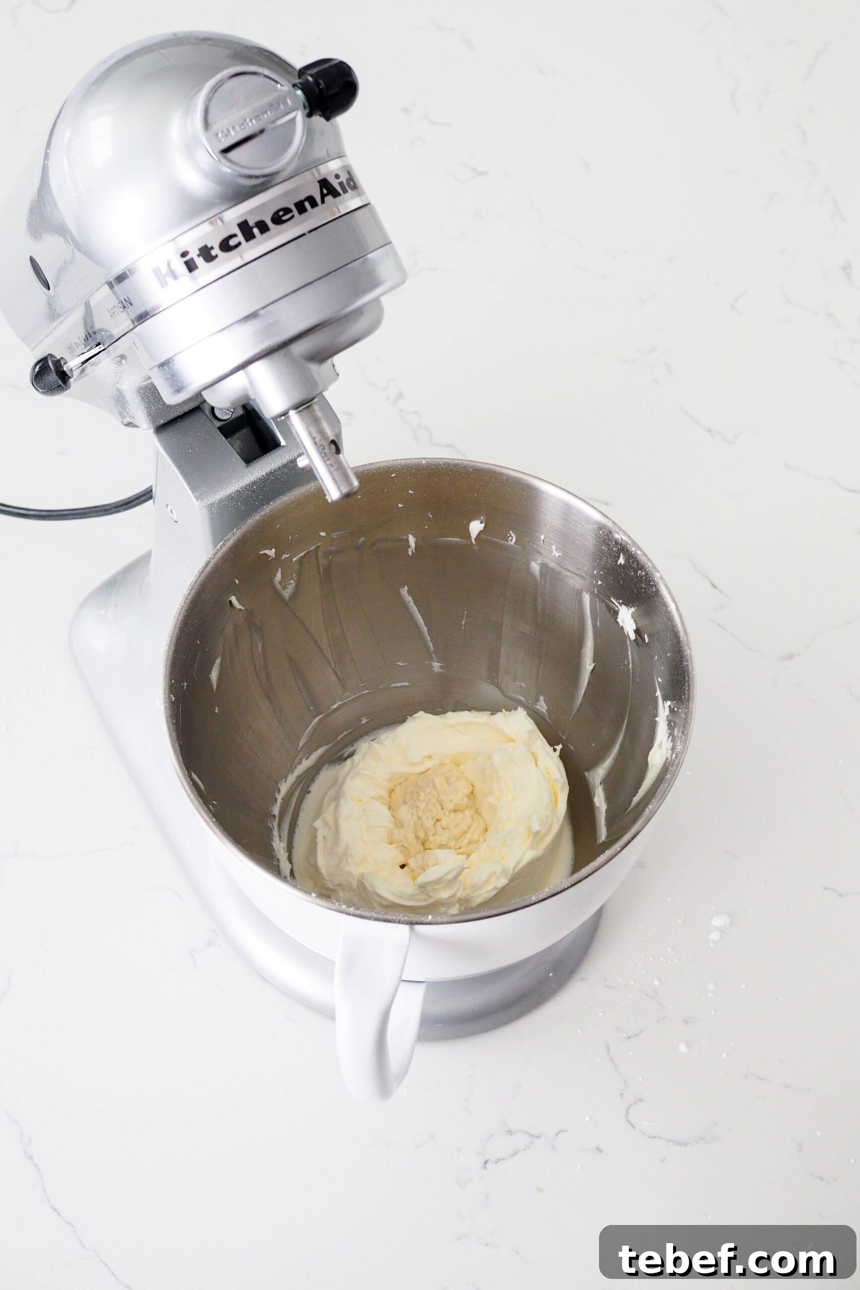 White Chocolate and Pomegranate Layer Cake Recipe 10 White chocolate is in a well inside of buttercream in a mixer bowl.