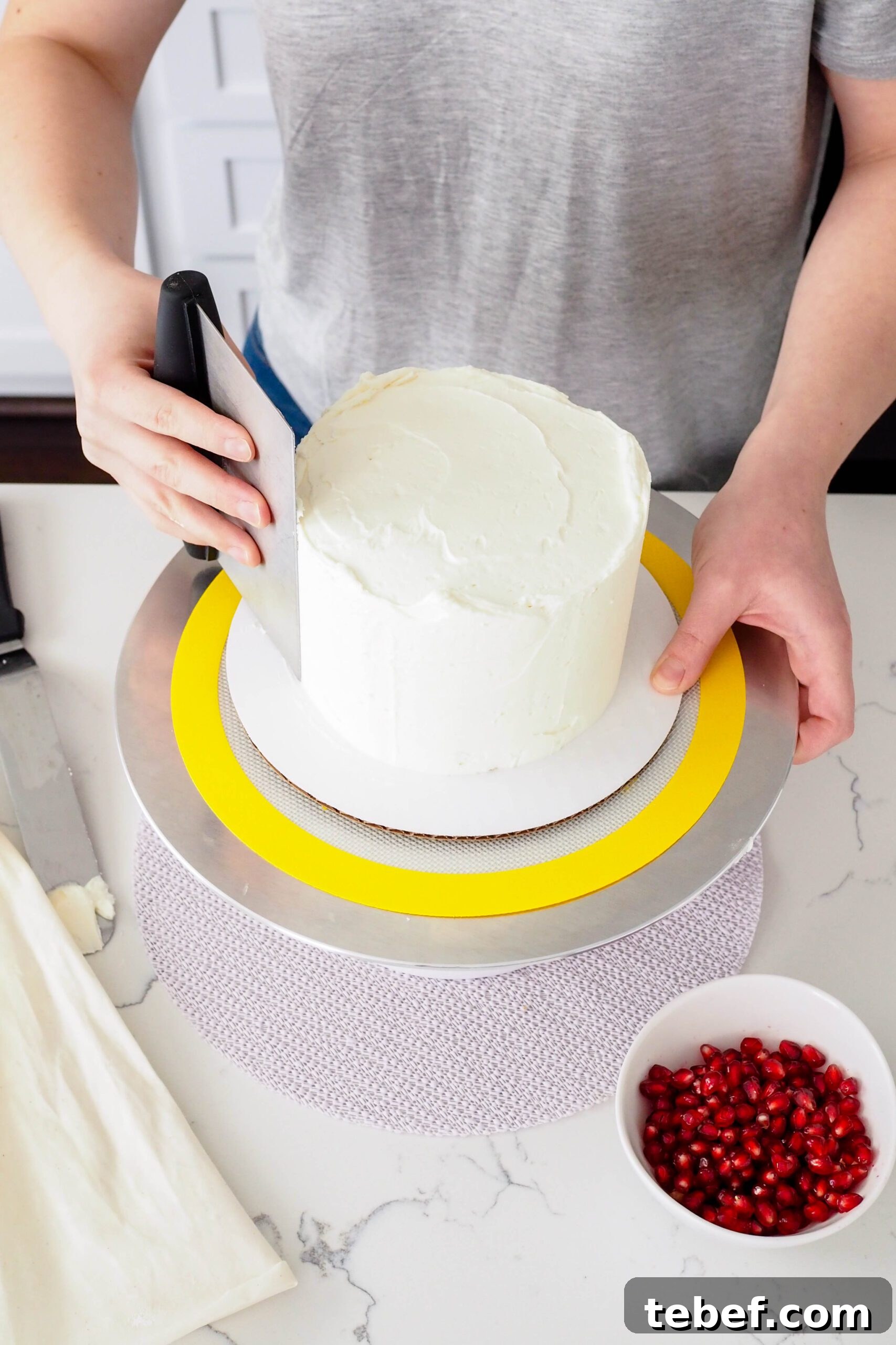White Chocolate and Pomegranate Layer Cake Recipe 13 A bench scraper smooths the sides of a 6" layer cake on a turntable.