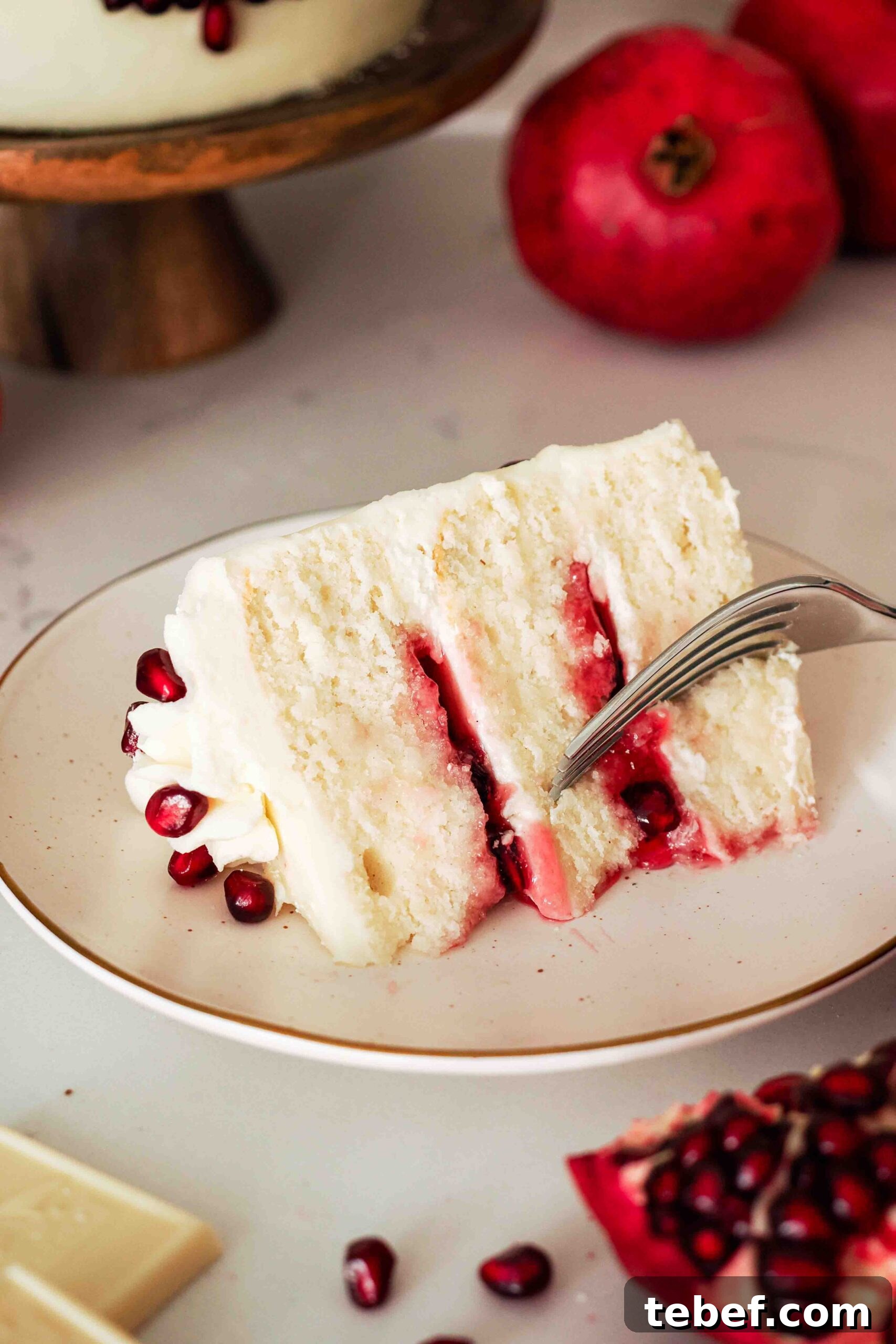 White Chocolate and Pomegranate Layer Cake Recipe 16 A slice of white chocolate pomegranate cake on its side and a fork taking a bite out of it.