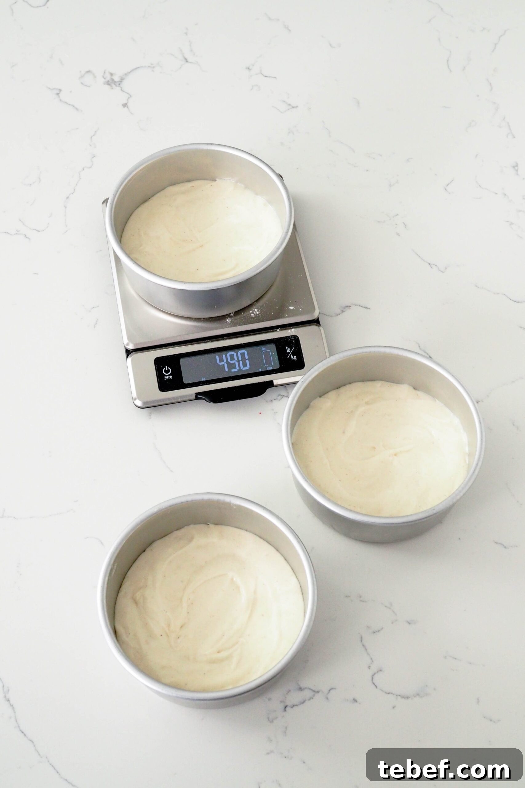 White Chocolate and Pomegranate Layer Cake Recipe 7 Three 6" cake pans are spread out on a counter, filled with cake batter. One rests on a scale.