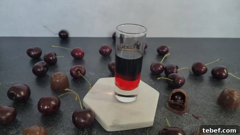 layered drink in a glass shot glass next to chocolate covered cherries