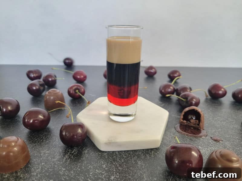 three layer drink in a glass shot glass next to chocolate covered cherries