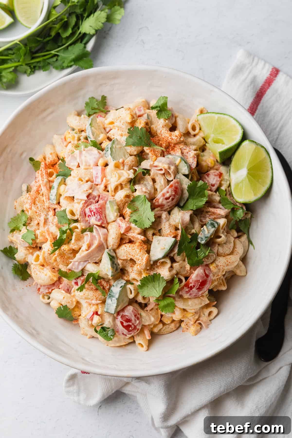 Mexican Macaroni Salad with Ham and Creamy Pepita Dressing 2 Mexican macaroni salad recipe in a white bowl with lime wedges and cilantro leaves.