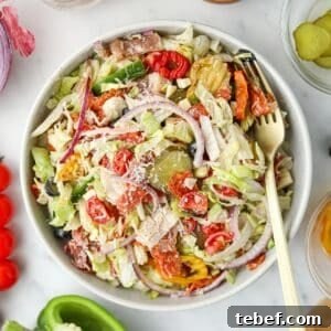 Italian Sub Sandwich Salad: Classic Deli Salad with Salami, Provolone & Italian Dressing 8 A bowl filled with salad, topped with pickles, red onion, cherry tomatoes, and a sprinkle of parmesan cheese.