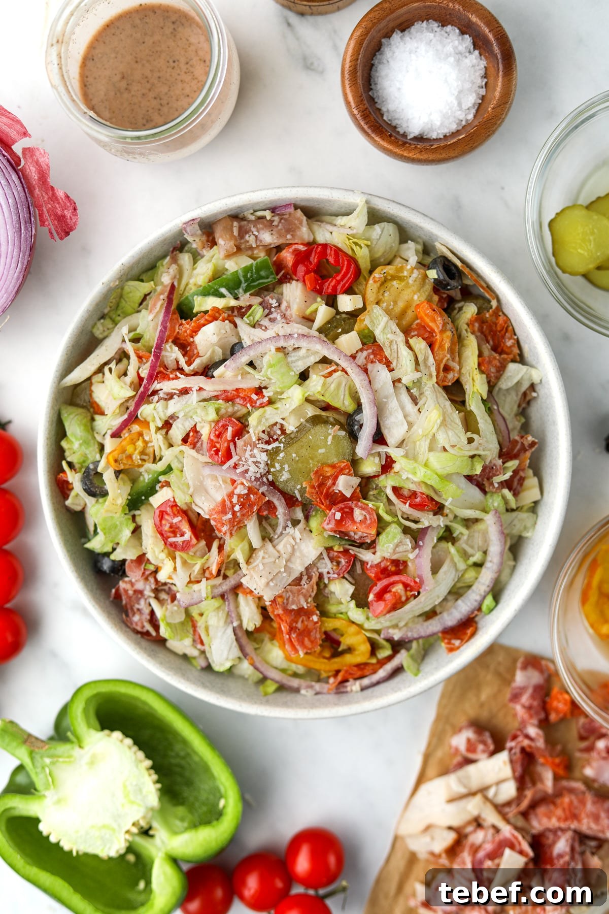 Italian Sub Sandwich Salad: Classic Deli Salad with Salami, Provolone & Italian Dressing 5 An overhead image of a bowl of salad, surrounded by vegetables and other various toppings.