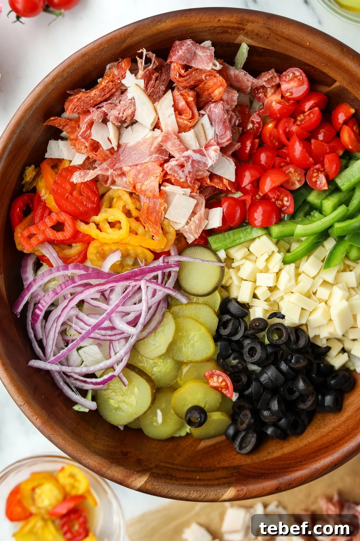 Italian Sub Sandwich Salad: Classic Deli Salad with Salami, Provolone & Italian Dressing 7 An overhead image of a large salad bowl filled with sections of toppings, including meat, cheese, pickles, etc.