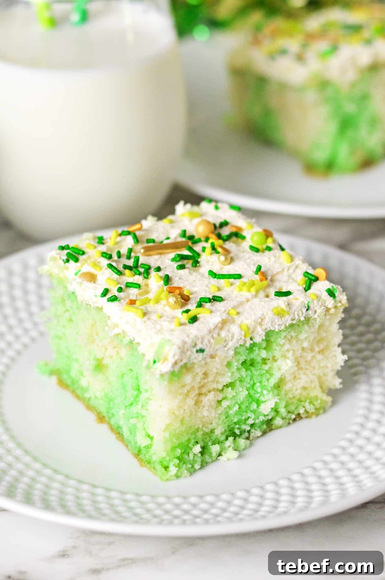 A slice of lime jello poke cake on a small white plate, decorated with St. patrick's day sprinkles.