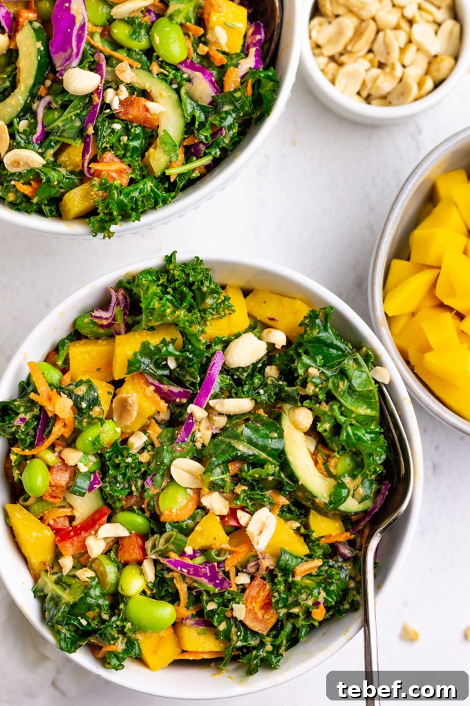 Thai Kale Salad with Creamy Peanut Dressing 2 kale Thai salad in white bowls with mango and peanuts in bowls nearby.