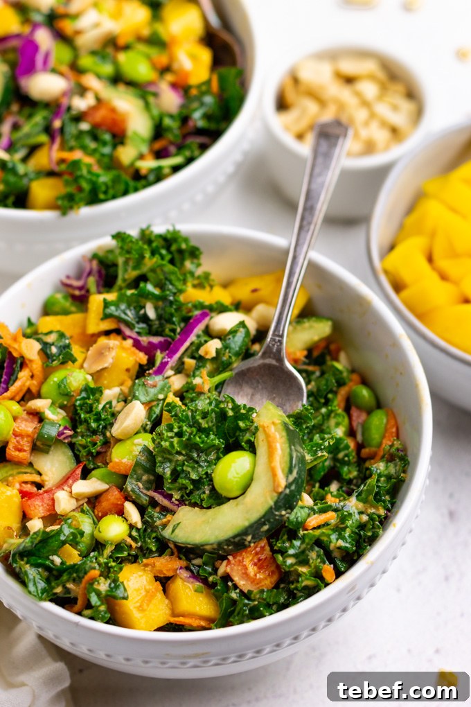Thai Kale Salad with Creamy Peanut Dressing 11 kale Thai salad in a bowl with a fork serving up some of the salad. Mango and peanuts are in separate bowls surrounding it.